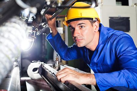 Das Bild zeigt einen Industriemeister bei der Überprüfung einer metallverarbeitenden Maschine.