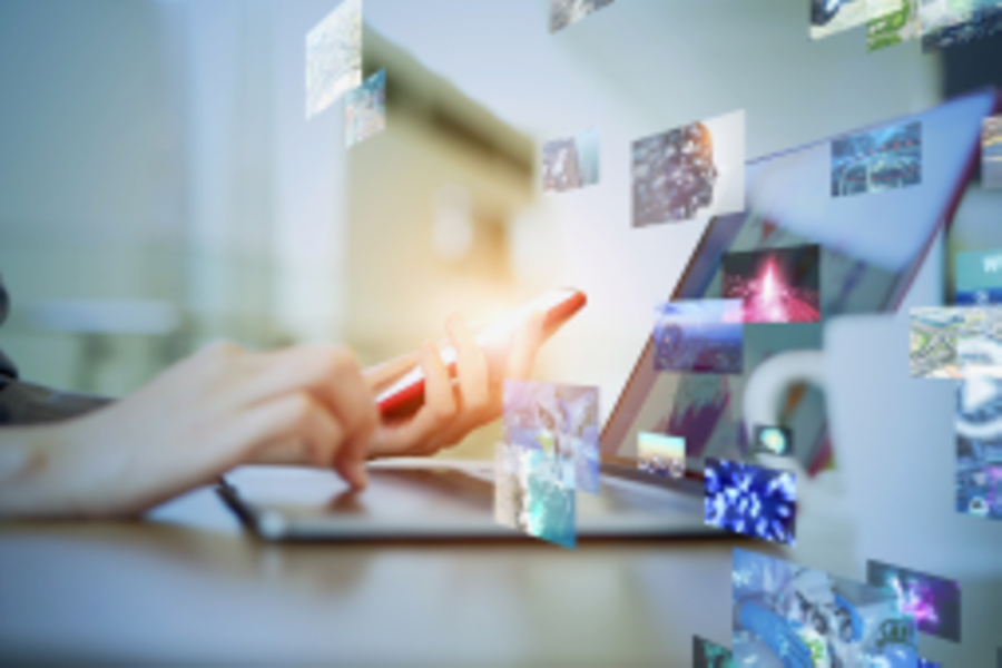 Das Bild zeigt eine Person, die mit einem Handy und Laptop arbeitet. Ebenfalls sind viele verschiedene Fotos zu sehen.