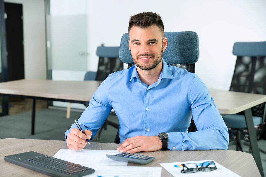 Das Bild zeigt einen Geschäftsmann an seinem Schreibtisch mit Tastatur, Taschenrechner und Unterlagen