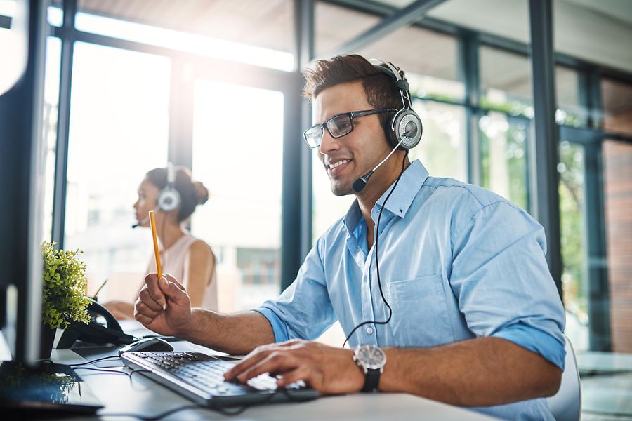 Das Bild zeigt einen Mitarbeiter mit einem Headset, der vor einem PC sitzt und mit einem Lieferanten telefoniert.