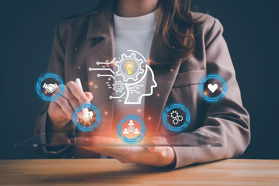 Das Bild zeigt im Vordergrund verschiedene KI Symbole. Im Hintergrund sitzt eine Geschäftsfrau mit einem Stift auf einen Symbol
