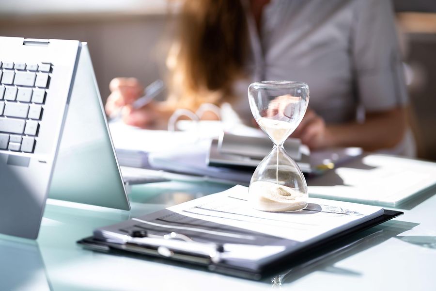 Das Bild zeigt einen Schreibtisch mit Unterlagen und Laptop, an dem eine Geschäftsfrau arbeitet